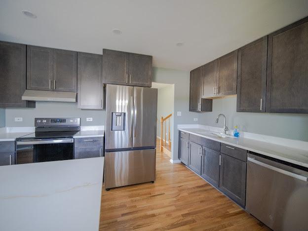 kitchen with a sink, under cabinet range hood, appliances with stainless steel finishes, light wood finished floors, and light countertops