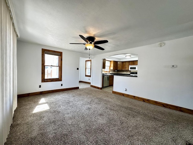 unfurnished living room with arched walkways, light colored carpet, a textured ceiling, and baseboards