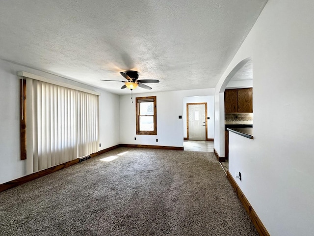 unfurnished living room with visible vents, arched walkways, carpet, and a textured ceiling