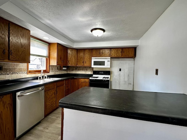 kitchen featuring gas stove, white microwave, a sink, dishwasher, and dark countertops