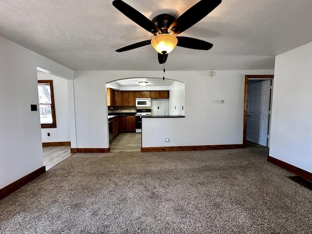 unfurnished living room featuring light carpet, a textured ceiling, arched walkways, baseboards, and ceiling fan