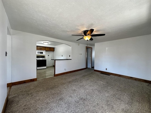 unfurnished living room with visible vents, baseboards, carpet, arched walkways, and a ceiling fan