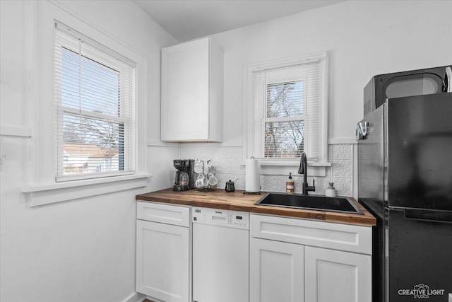 kitchen featuring a wealth of natural light, a sink, freestanding refrigerator, white dishwasher, and wooden counters