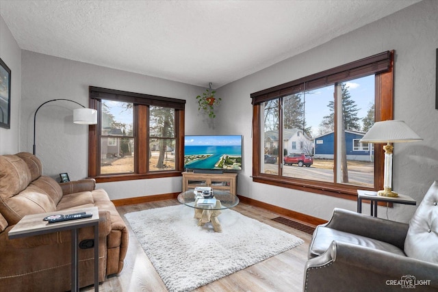 living area featuring visible vents, a textured ceiling, baseboards, and wood finished floors