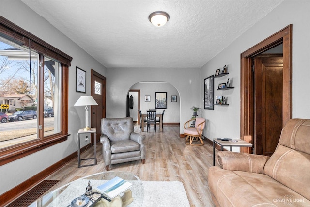 living area featuring arched walkways, light wood finished floors, a textured ceiling, and baseboards