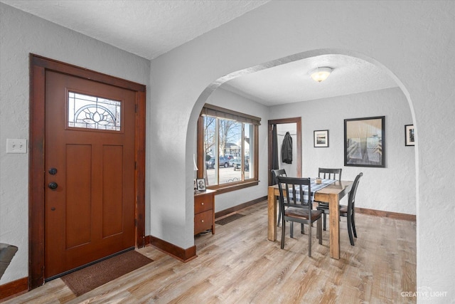 dining area with arched walkways, a textured ceiling, and light wood-type flooring