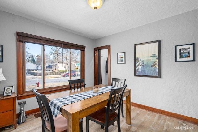 dining space with light wood-type flooring, baseboards, a textured ceiling, and a textured wall