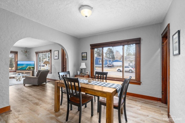 dining area featuring arched walkways, baseboards, light wood-style floors, and a textured wall