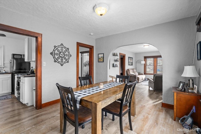 dining area with baseboards, arched walkways, a textured ceiling, and light wood finished floors