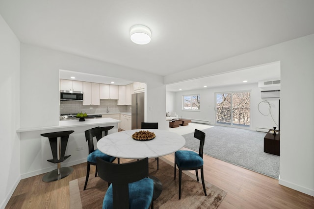 dining space with a baseboard heating unit, light wood-style floors, and baseboards