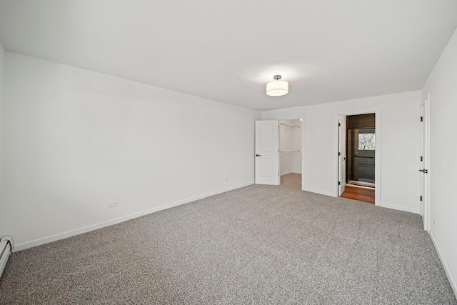 unfurnished bedroom with a spacious closet, baseboards, carpet, a closet, and a baseboard radiator