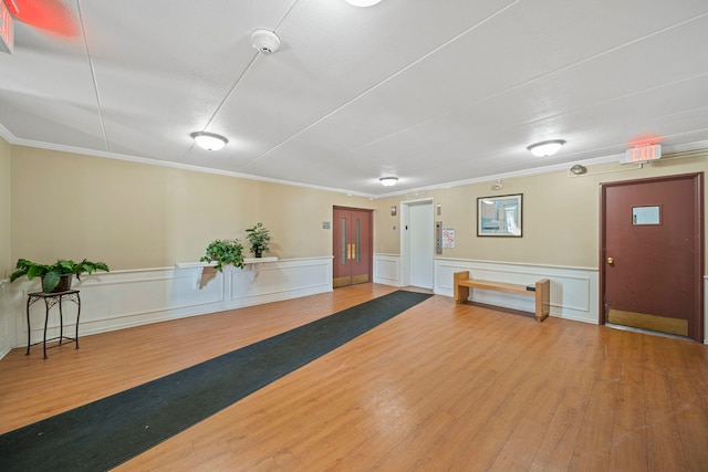 exercise area featuring wood finished floors, a wainscoted wall, and ornamental molding