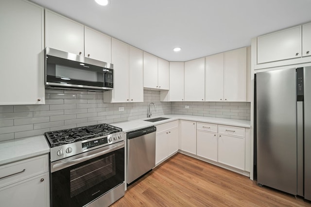 kitchen with tasteful backsplash, light countertops, light wood-style flooring, appliances with stainless steel finishes, and a sink