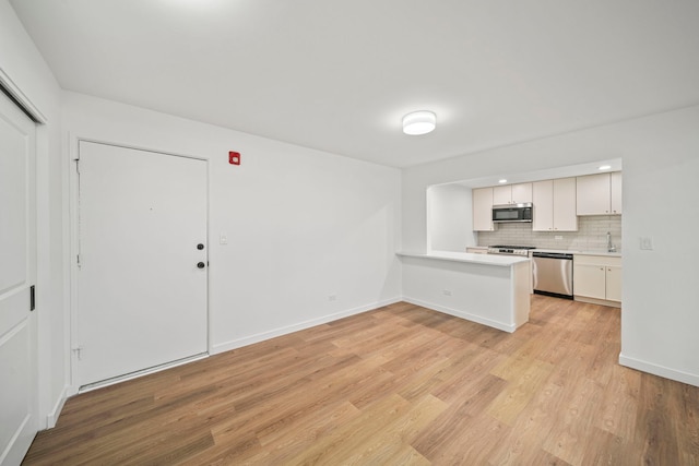 kitchen with light wood-type flooring, backsplash, appliances with stainless steel finishes, a peninsula, and light countertops