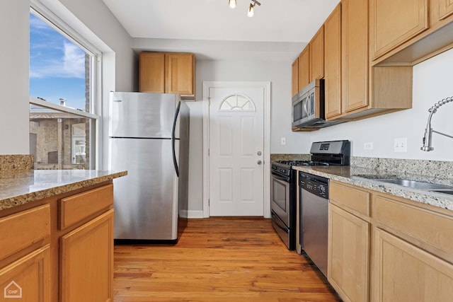 kitchen with a sink, light wood-style flooring, light stone countertops, and stainless steel appliances