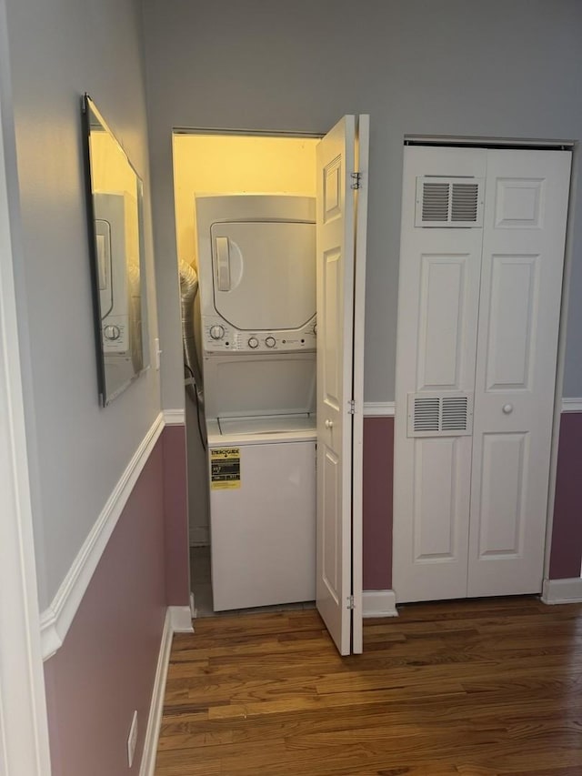 washroom with visible vents, wood finished floors, stacked washing maching and dryer, baseboards, and laundry area