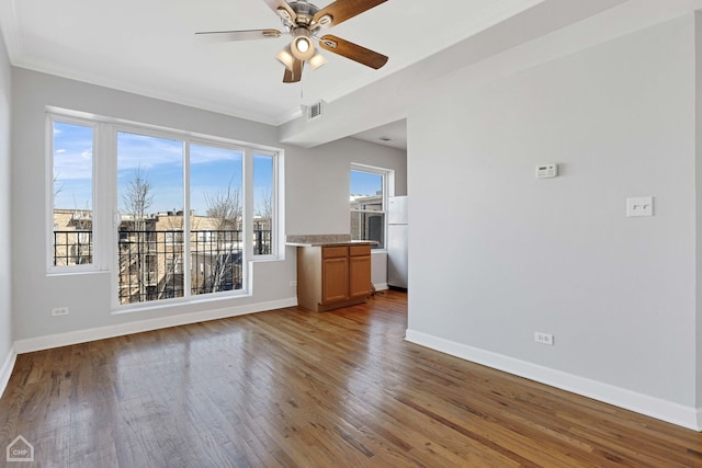 unfurnished living room with visible vents, baseboards, ornamental molding, a ceiling fan, and wood-type flooring