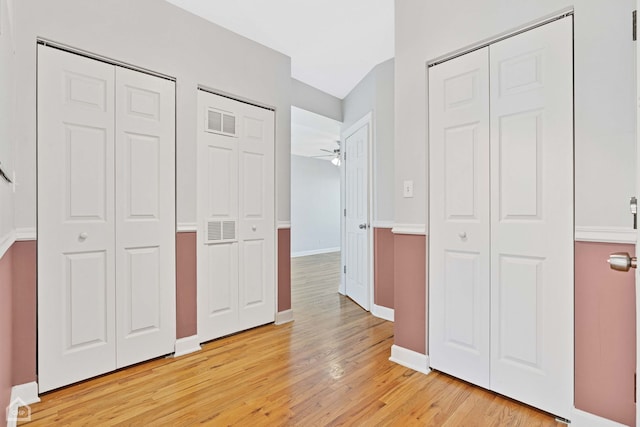 unfurnished bedroom featuring two closets, visible vents, baseboards, and light wood finished floors