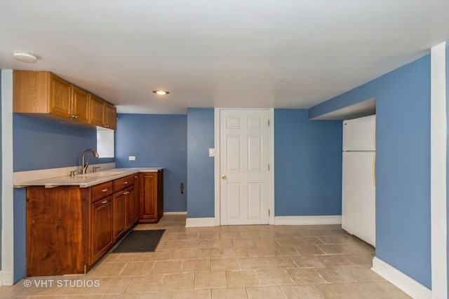 kitchen featuring light countertops, baseboards, freestanding refrigerator, and a sink