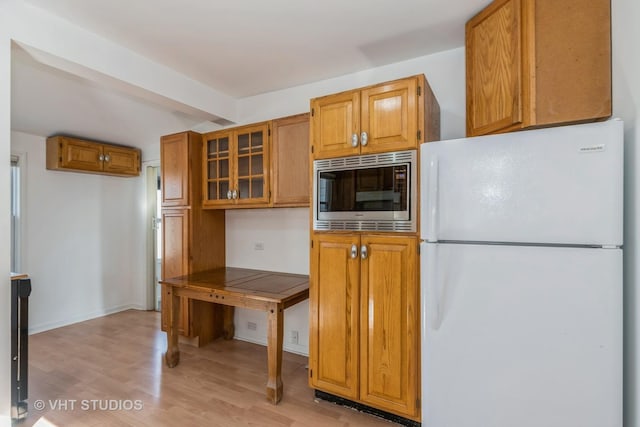 kitchen with stainless steel microwave, glass insert cabinets, light wood-style flooring, freestanding refrigerator, and brown cabinetry