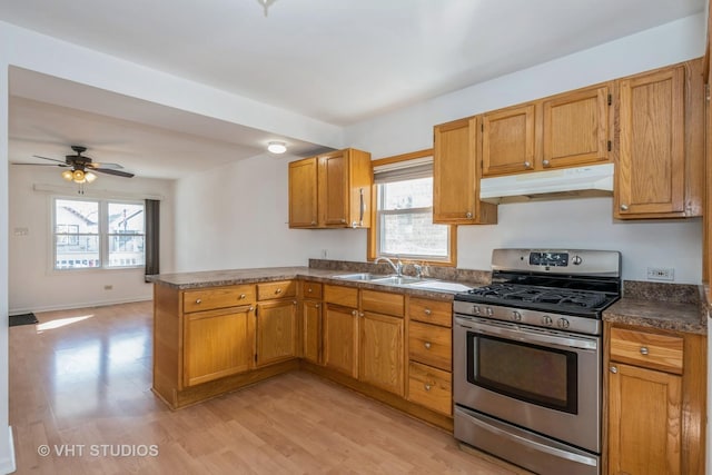 kitchen featuring dark countertops, under cabinet range hood, gas range, a peninsula, and a sink