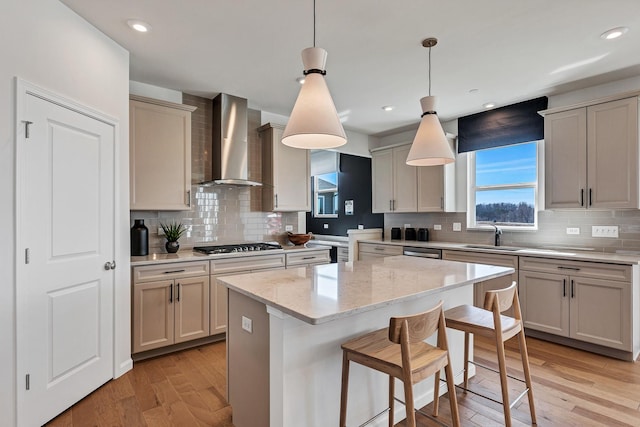 kitchen with a breakfast bar area, wall chimney exhaust hood, light wood-style floors, and a center island