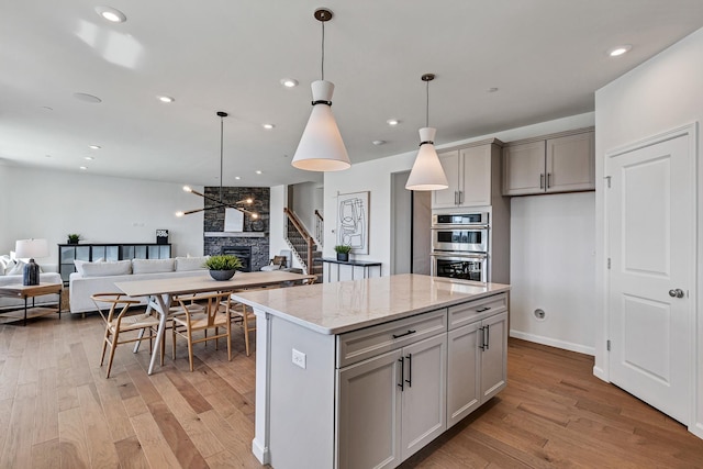 kitchen with light stone counters, gray cabinets, open floor plan, and light wood finished floors