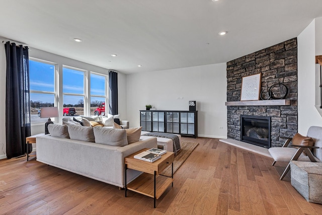 living room featuring a stone fireplace, recessed lighting, wood finished floors, and baseboards