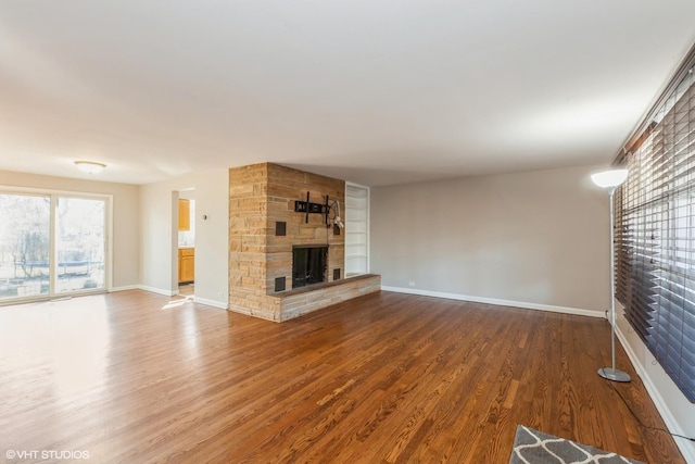 unfurnished living room with a stone fireplace, baseboards, and wood finished floors