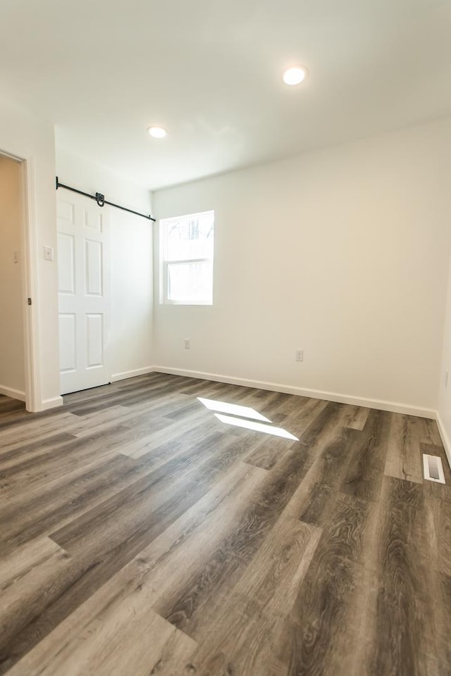 unfurnished bedroom featuring visible vents, wood finished floors, recessed lighting, a barn door, and baseboards