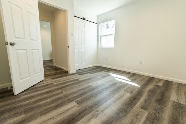 unfurnished bedroom featuring a closet, baseboards, dark wood-type flooring, and a barn door