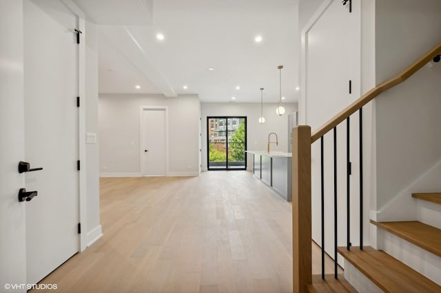 hallway featuring baseboards, recessed lighting, a sink, stairs, and light wood-style floors