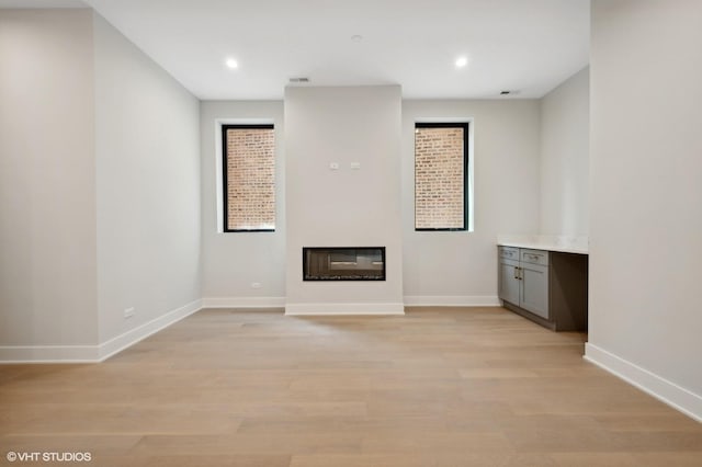 unfurnished living room featuring a glass covered fireplace, light wood-style flooring, visible vents, and baseboards