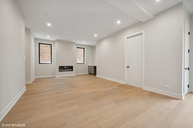 below grade area with light wood finished floors, a glass covered fireplace, and recessed lighting