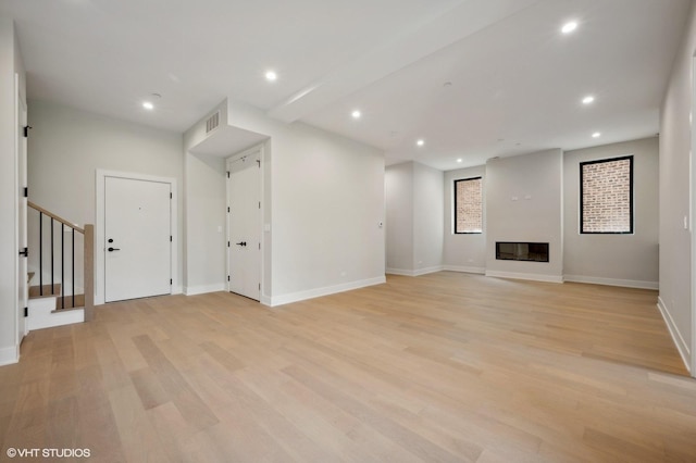 unfurnished living room with a glass covered fireplace, stairway, recessed lighting, and light wood-type flooring