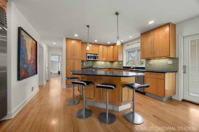 kitchen with a sink, appliances with stainless steel finishes, dark countertops, and light wood finished floors