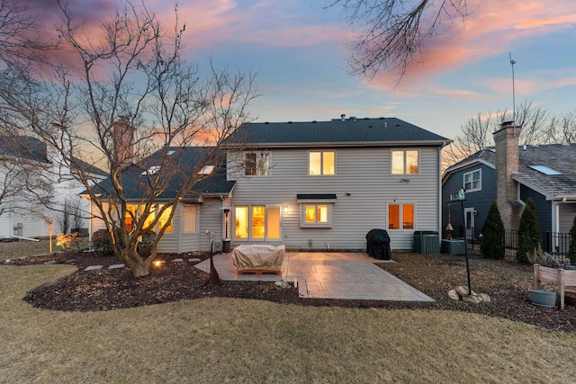 back of house at dusk with a patio, central air condition unit, fence, and a lawn