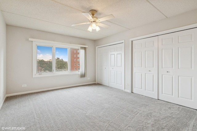 unfurnished bedroom with multiple closets, a textured ceiling, carpet floors, baseboards, and ceiling fan