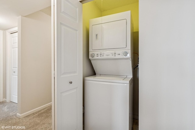 laundry area with laundry area, light colored carpet, stacked washer and clothes dryer, and baseboards