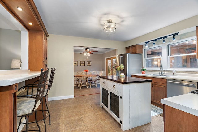 kitchen with light tile patterned floors, brown cabinetry, a sink, stainless steel appliances, and a kitchen bar