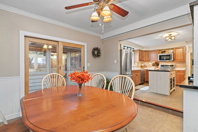 dining area featuring crown molding, light tile patterned flooring, a ceiling fan, and a wainscoted wall