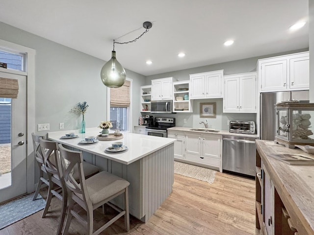 kitchen with light countertops, light wood-style flooring, white cabinets, stainless steel appliances, and a sink