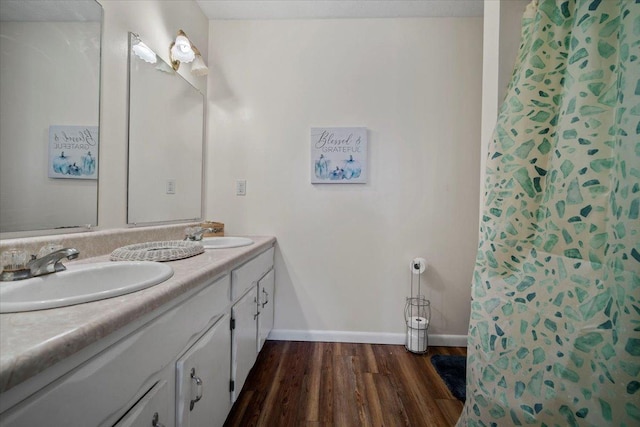 bathroom featuring double vanity, wood finished floors, baseboards, and a sink