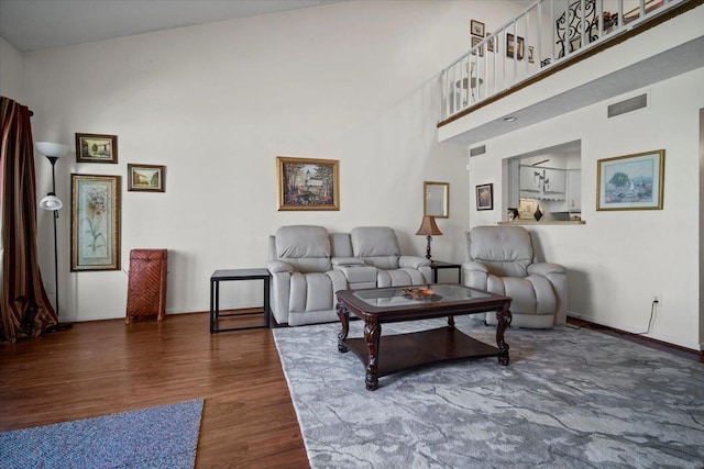 living room featuring visible vents, a towering ceiling, baseboards, and wood finished floors