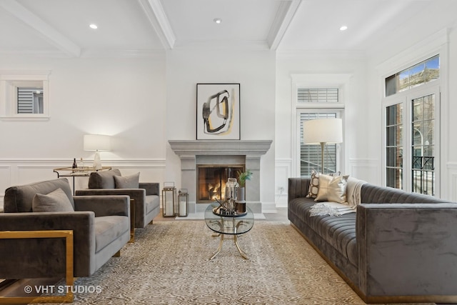 living room featuring beamed ceiling, plenty of natural light, a decorative wall, and a glass covered fireplace