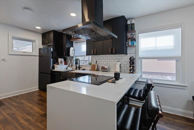 kitchen featuring a sink, light countertops, dark wood-type flooring, tasteful backsplash, and island range hood