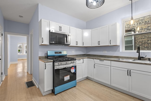 kitchen featuring visible vents, a sink, stainless steel appliances, white cabinets, and light wood-type flooring