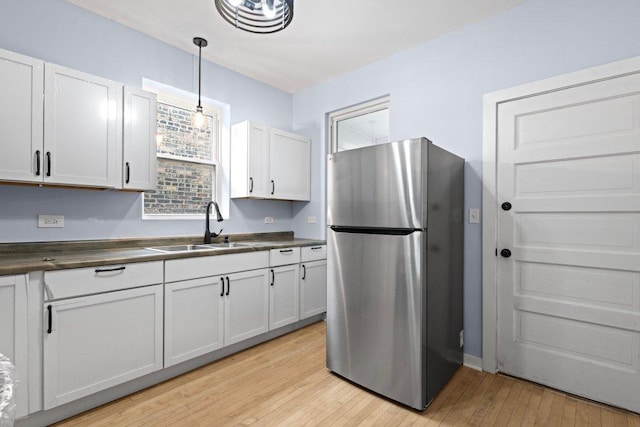 kitchen featuring pendant lighting, a sink, dark countertops, freestanding refrigerator, and light wood finished floors