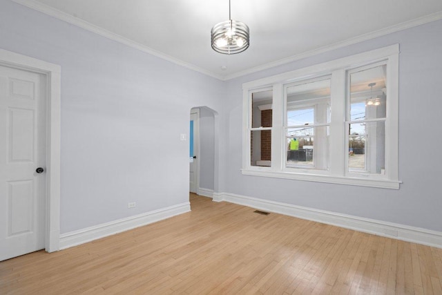 spare room with visible vents, crown molding, baseboards, light wood-style floors, and arched walkways