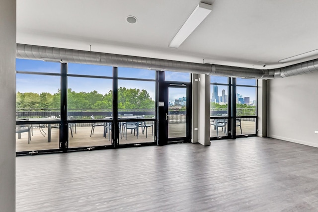 unfurnished room featuring a city view, floor to ceiling windows, wood finished floors, and baseboards